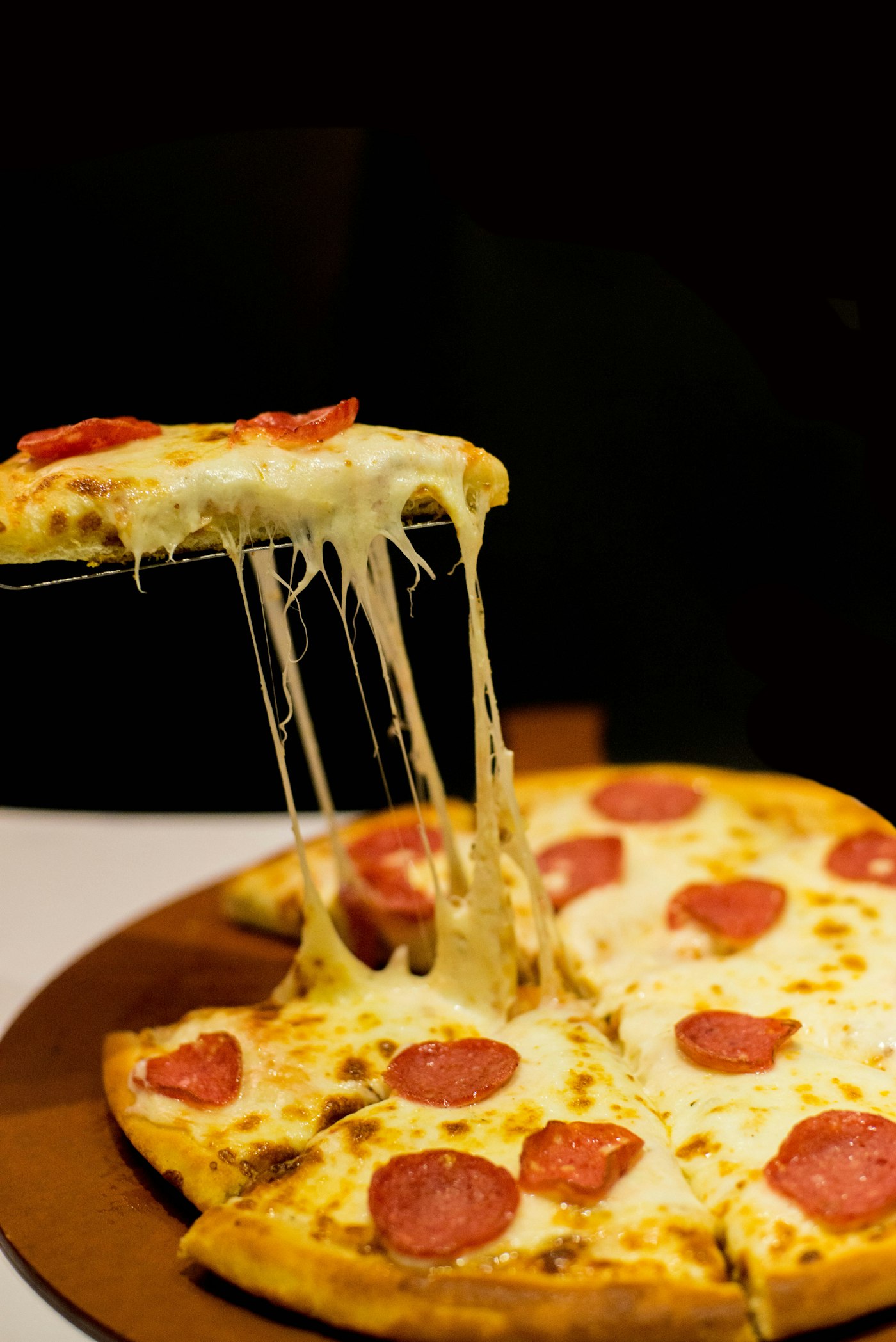 Pepperoni pizza slice with a long cheese pull, fresh from the Cheese O'Clock oven