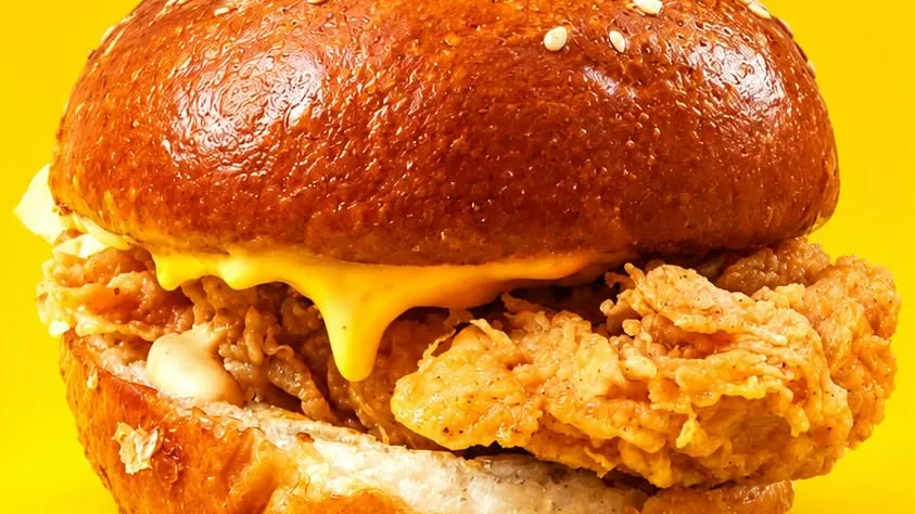 A crispy chicken burger with melted cheese in a brioche bun, up close